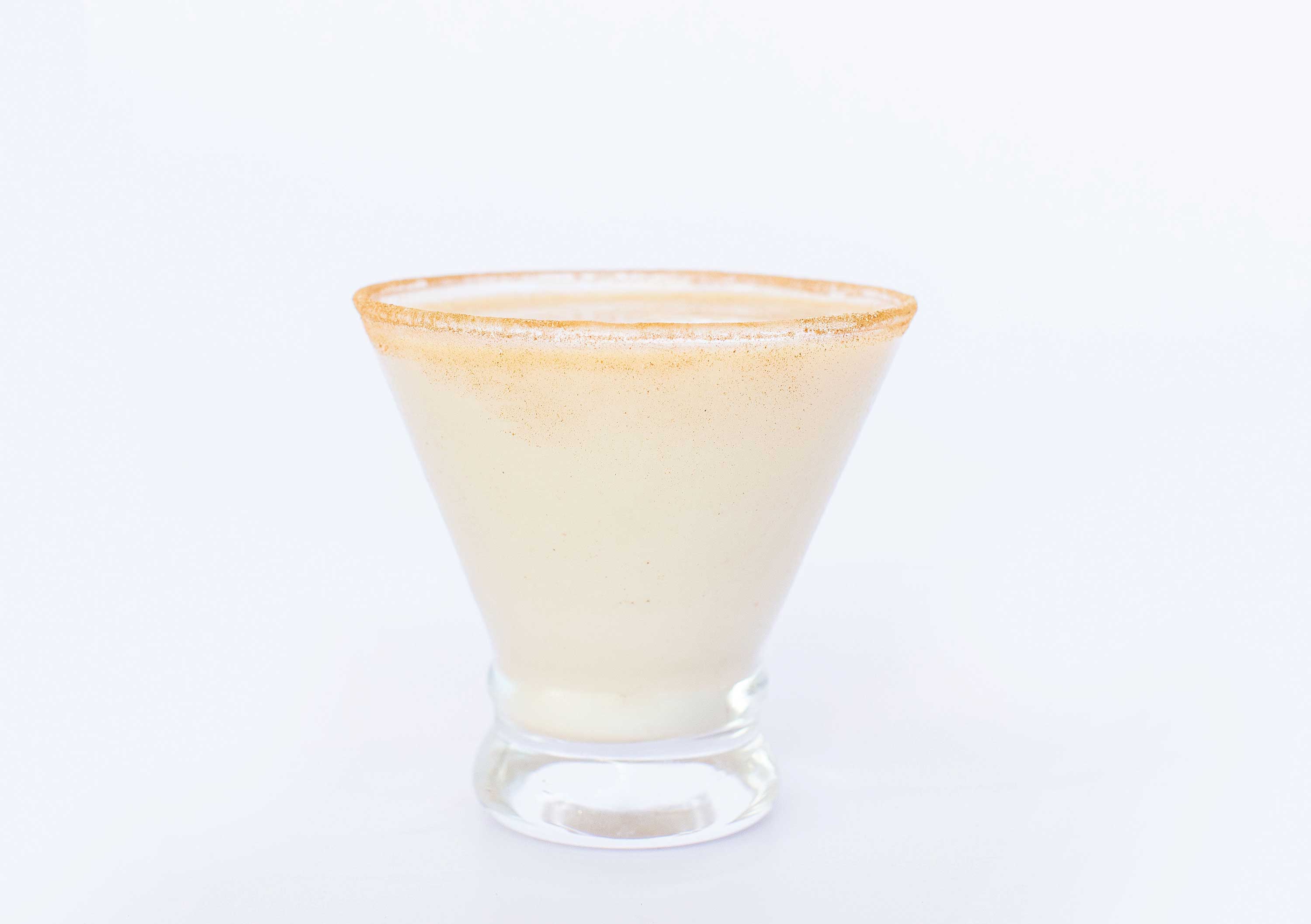 Image: A flared glass is filled with a creamy white liquid. There is a light dusting of cinnamon powder on the rim.